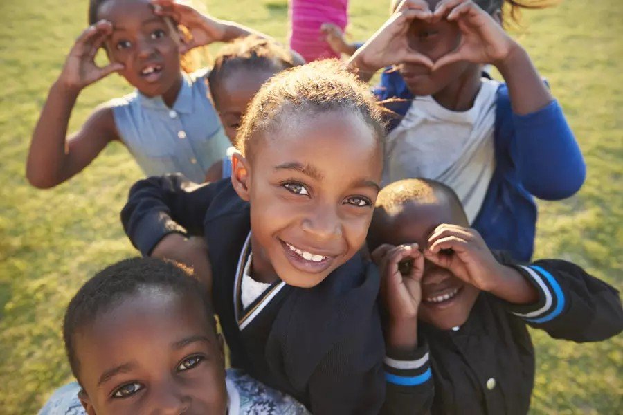 A group of smiling children making heart shapes with their hands